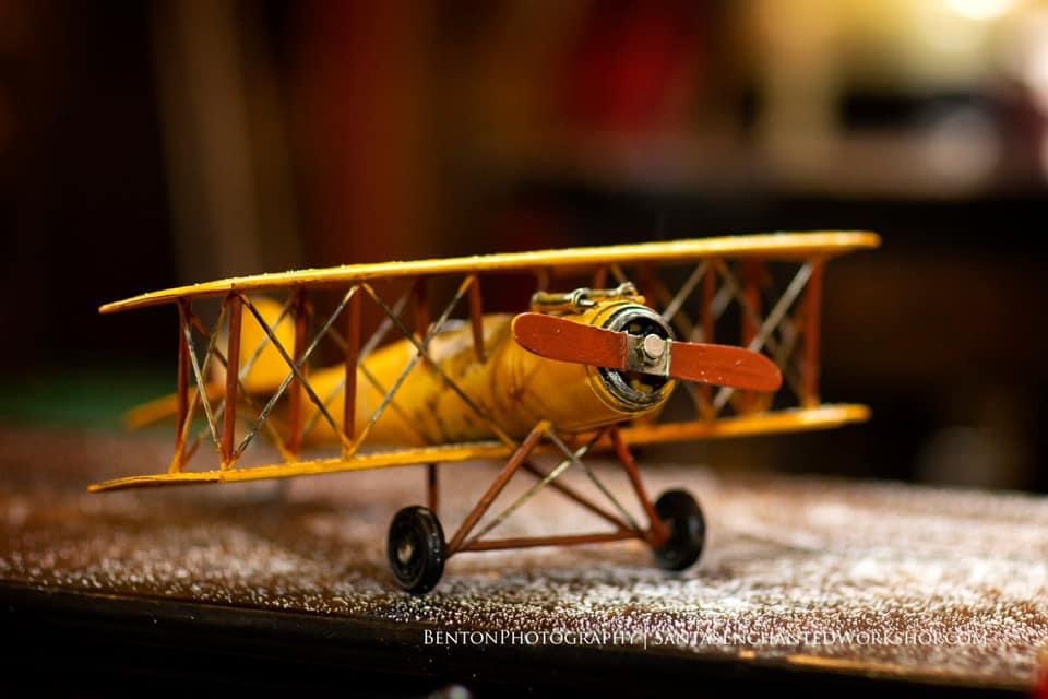 A yellow tin biplane parked on a glittering workshop shelf