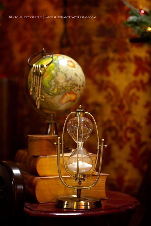 An antique globe hung with brass keys beside a turning hourglass, in the workshop's candlelight