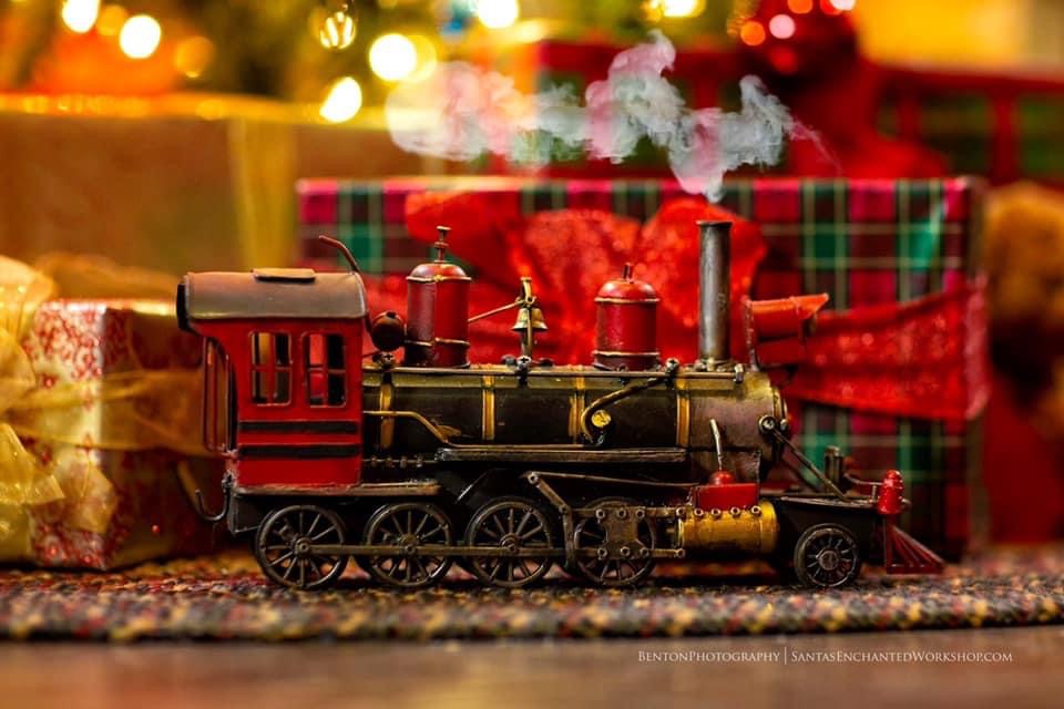 A tin toy locomotive with smoke curling from its stack, beneath the tree
